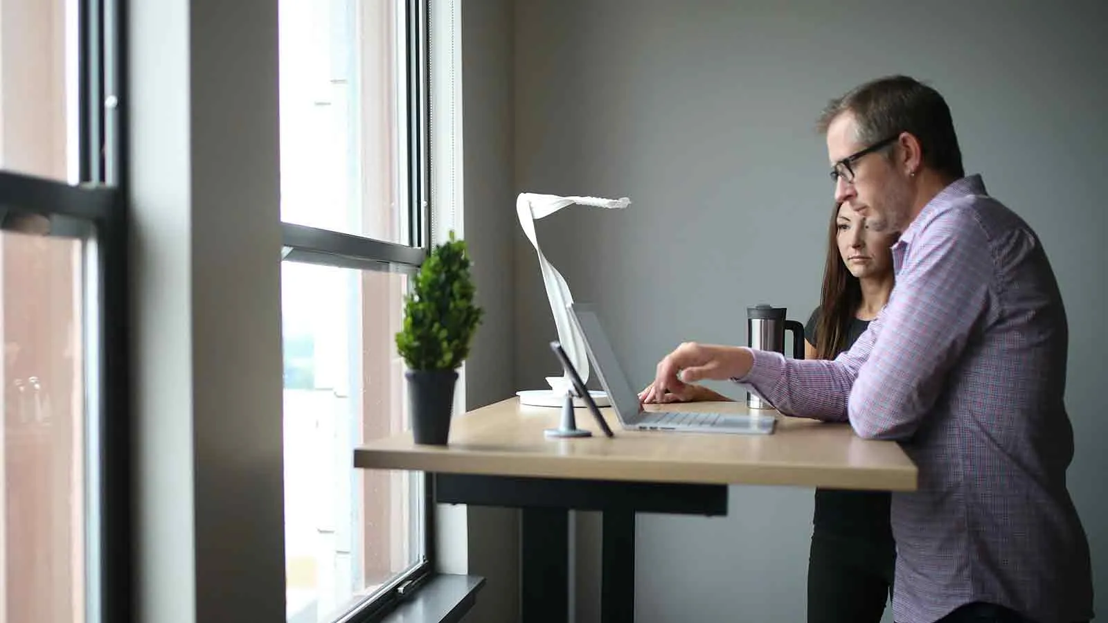 Two people at a standing desk reviewing a document on a laptop by a window, the record review stage that follows an ancient mortgage turning up