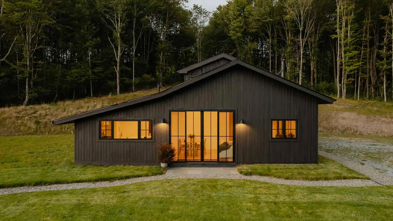 A dark-stained house at dusk in a clearing at the edge of woodland, the sort of long-held rural parcel where an unreleased mortgage from the 1960s tends to surface