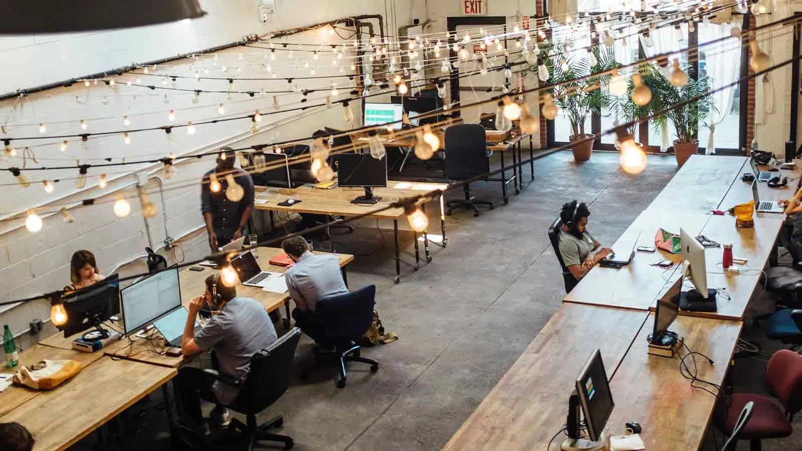 An open-plan office with long shared desks, monitors and strings of hanging bulbs, the kind of workout group that decides whether a deed in lieu is cheaper than a foreclosure