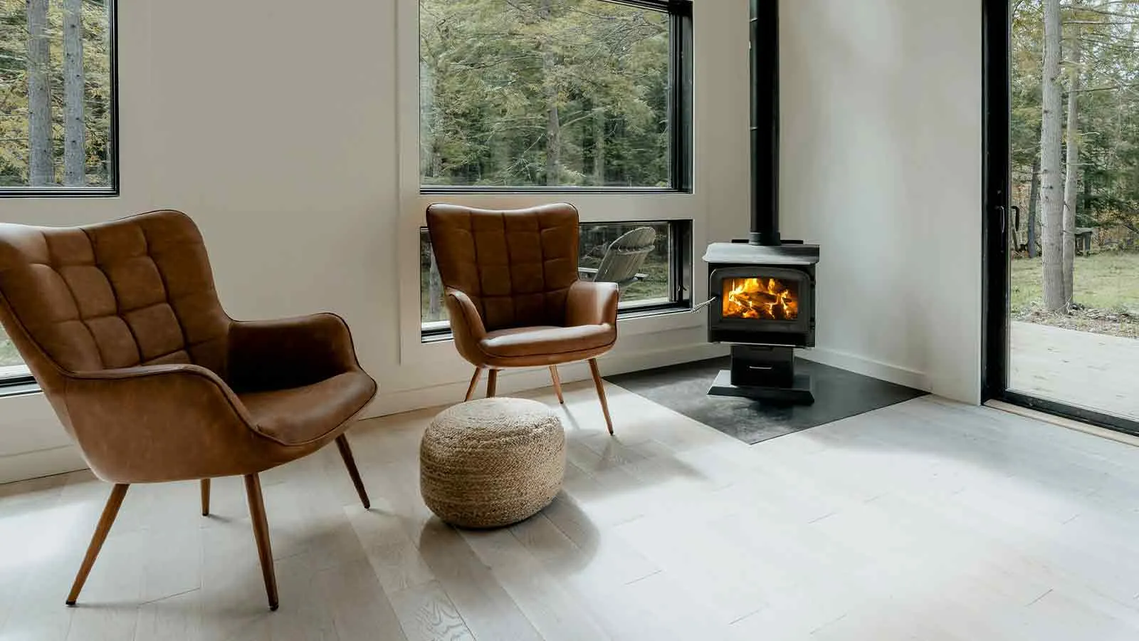 Two leather armchairs facing a wood stove in a bright room with forest visible through floor-to-ceiling windows, the kind of jointly occupied home whose ownership form decides which creditors can reach it